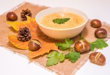 Schüssel mit Kastaniensuppe umgeben von Kastanien und Herbstlaub