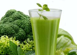 Ein Glas mit grünem Smoothie, daneben grünes Gemüse und frische Kräuter