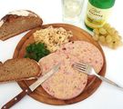 Holzteller mit Besteck, Saumagen, Brot, daneben eine Flasche Riesling und ein gefülltes Weinglas