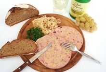 Holzteller mit Besteck, Saumagen, Brot, daneben eine Flasche Riesling und ein gefülltes Weinglas