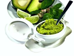 Schüsselchen mit Avocadocreme, eine aufgeschnittene Avocado und Limetten