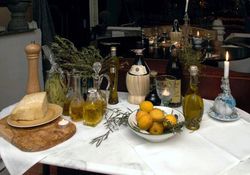 Tisch mit Ölflaschen, einer Schale Zitronen, brennende Kerze, Rotwein und Käse