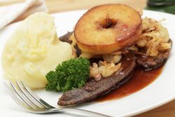 Teller mit Gabel und Kalbsleber sowie Kartoffelbrei, Apfelring und Petersilie