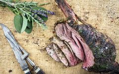 Gebratene Hirschkeule auf einem Holzbrett mit Messer und Fleischgabel