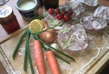 Holzbrett mit mehligen Kalbsbeinscheiben, zwei Karotten, einer Zwiebel, Tomaten, Knoblauch und Zitrone
