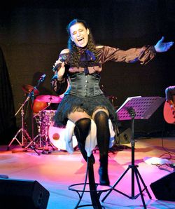 Julia Neigel singend und sitzend mit Mikrofon auf einer Bühne