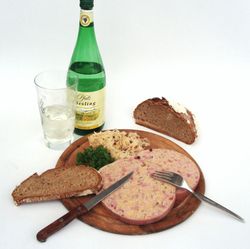 Holzteller mit Besteck, Saumagen, Brot, daneben eine Flasche Riesling und ein gefülltes Weinglas