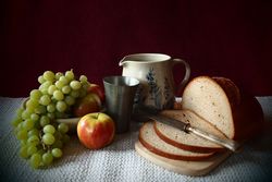 Brotzeit mit Trauben, Äpfeln, zum Teil aufgeschnittenem Brot, Krug und Zinnbecher