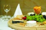 Holzteller mit Käse und Trauben und ein Weinglas